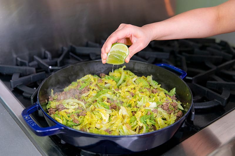 Squeezing fresh lime juice on a pan of Nom Nom Paleo's garbage stir-fry, filled with ground beef and curried cabbage.