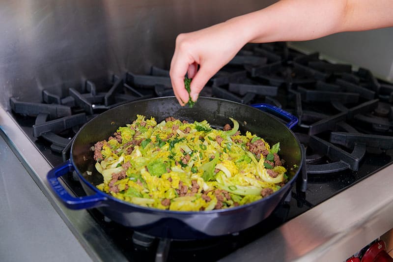 Sprinkling fresh herbs on a pan filled with Nom Nom Paleo garbage stir-fry.