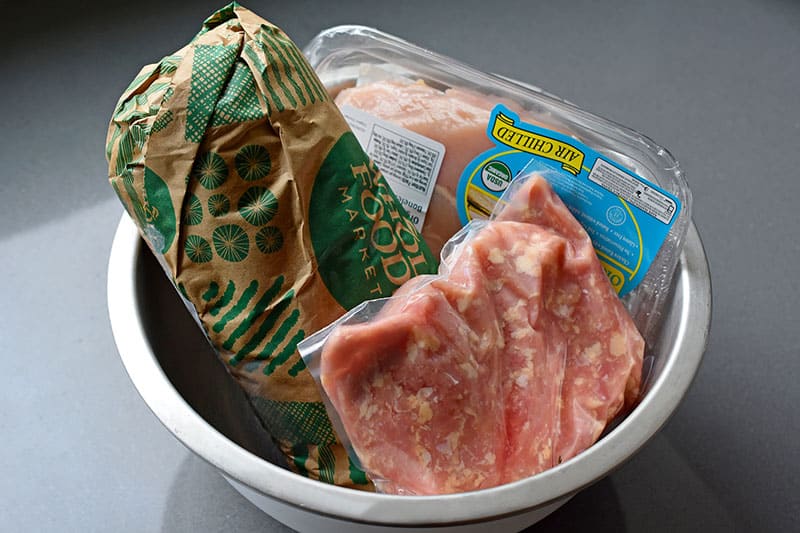 A metal bowl filled with packages of frozen meat that are thawing. This is Nom Nom Paleo's defrost bowl.
