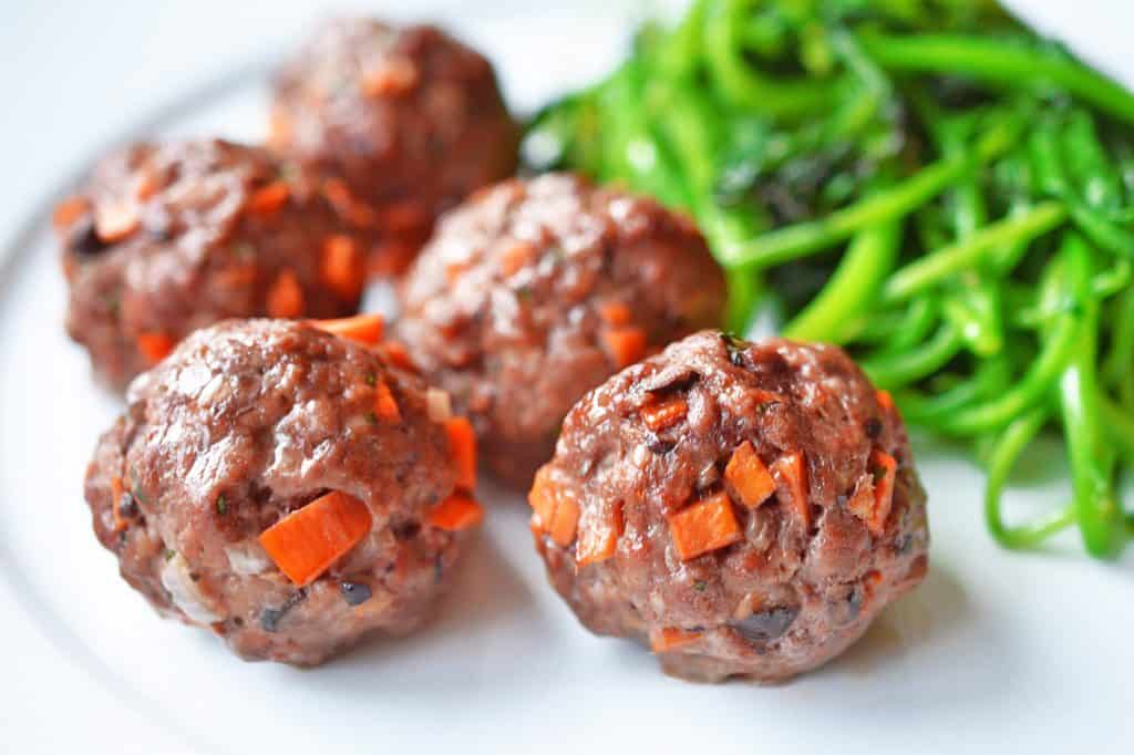 A plate of Asian Meatballs with some sautéed green vegetables on the side.
