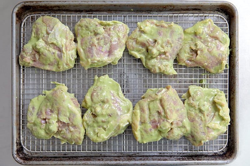 An overhead shot of marinated thighs arranged on a wire rack in a rimmed baking sheet with the skin-side down.