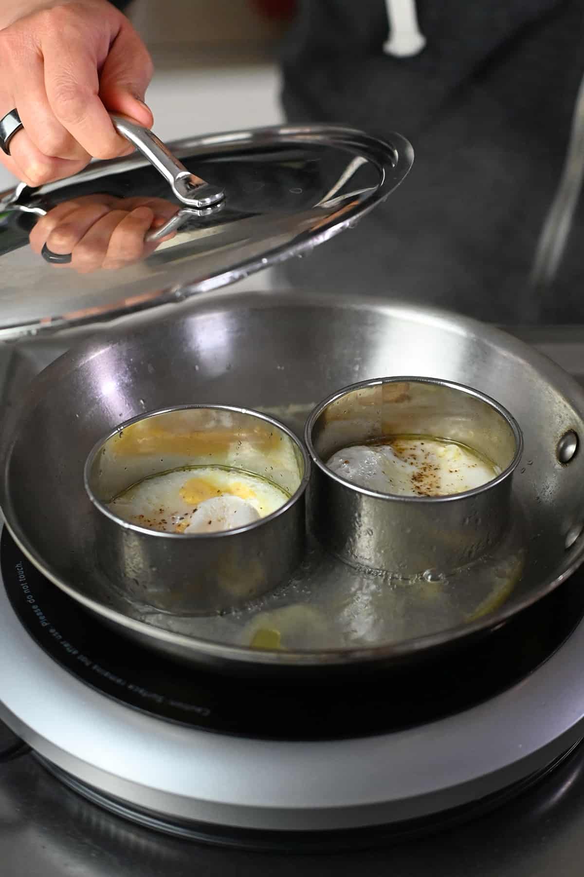 Removing the lid on a skillet filled with biscuit cutters and cooked eggs.