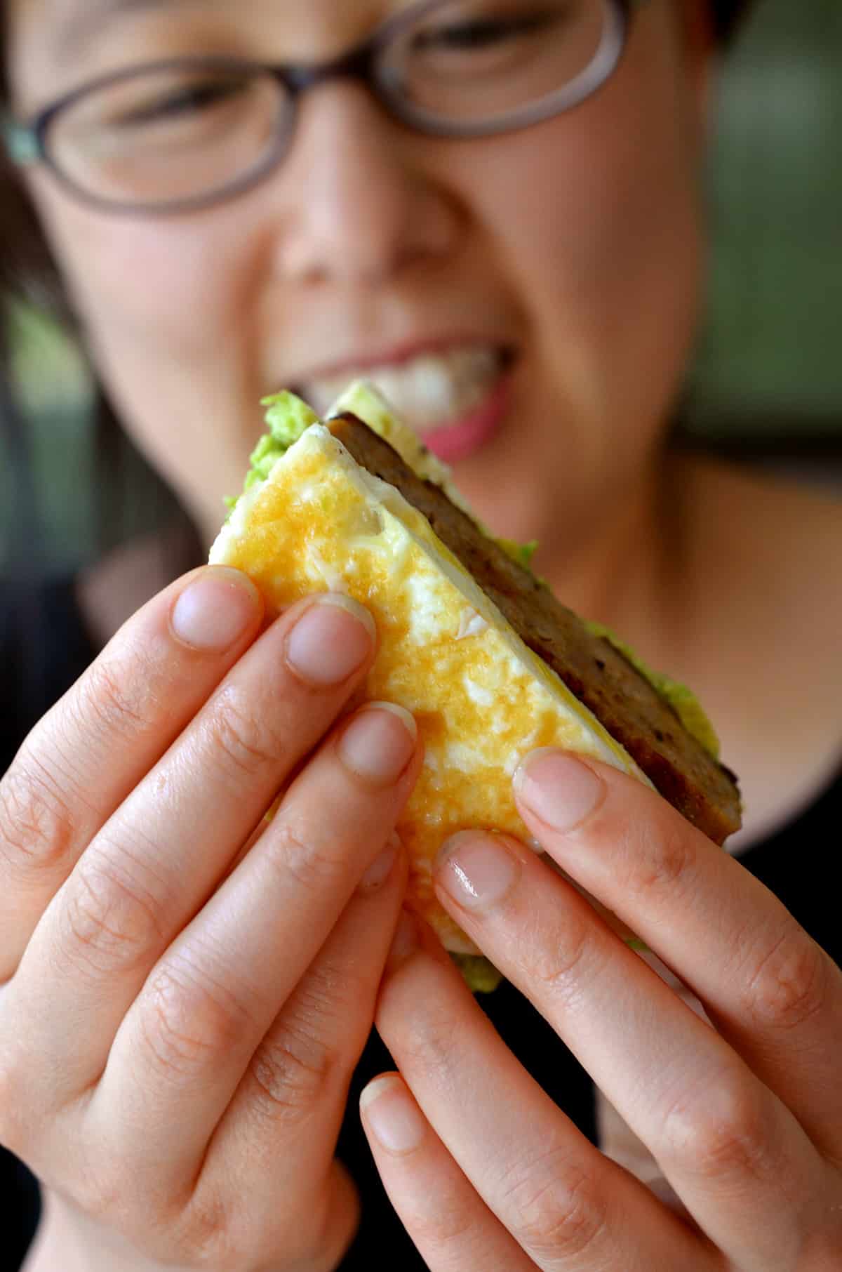 A smiling Asian woman is holding a paleo egg McMuffin.