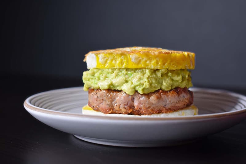 A side view of a Paleo Sausage Egg McMuffin on a white plate on a black background