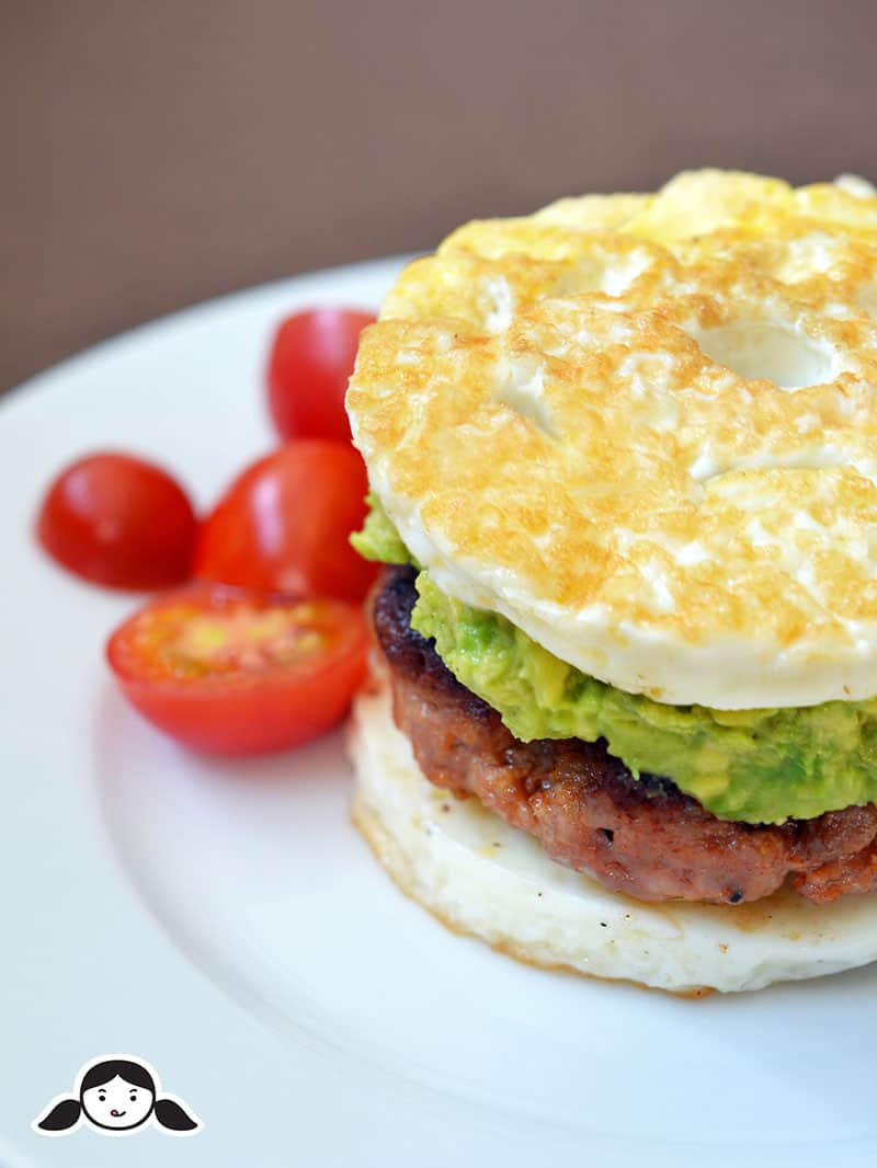 A closeup side shot of a keto and Paleo Sausage Egg McMuffin on a white plate with cherry tomatoes on the side