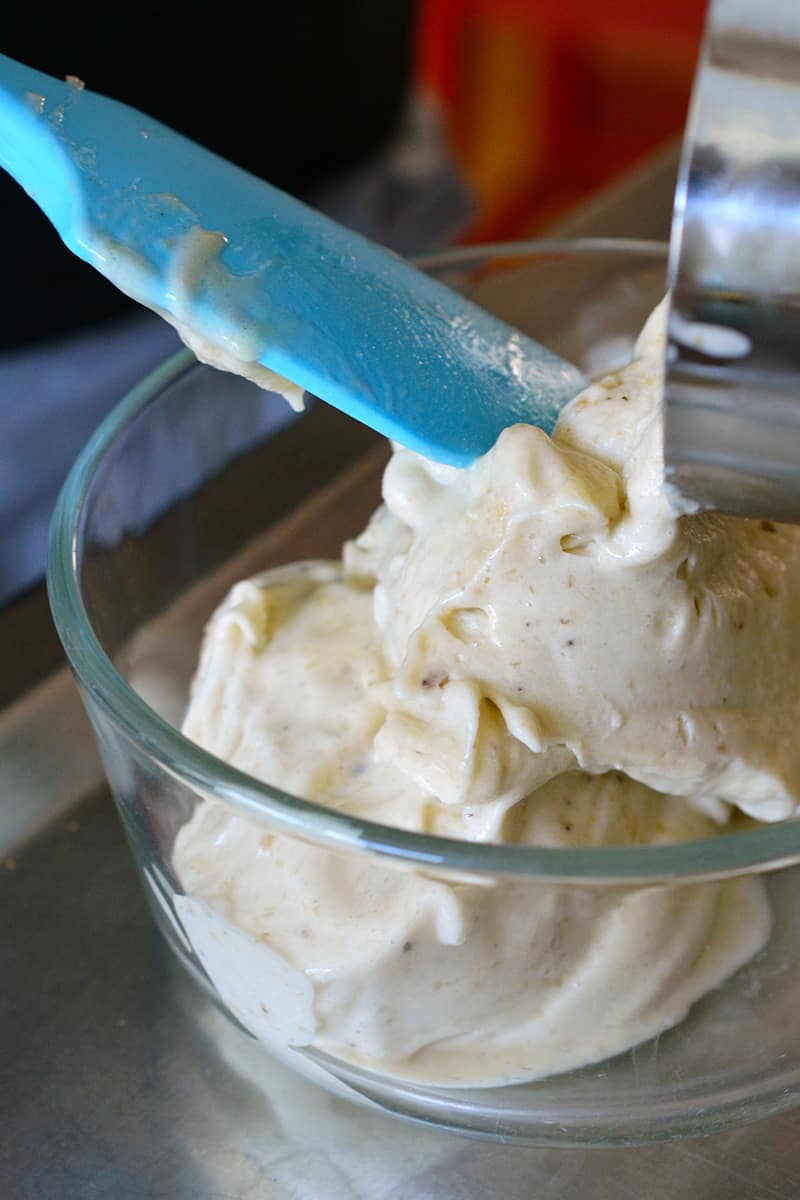 Transferring vegan banana ice cream to a class container with a blue silicone spatula.
