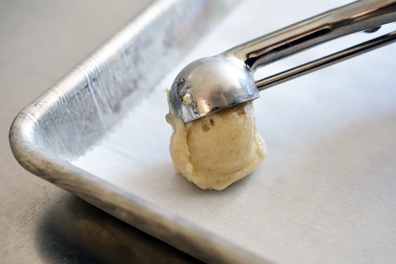 Using a small dishes to transfer vegan banana ice cream scoops on a parchment lined rimmed baking sheet.