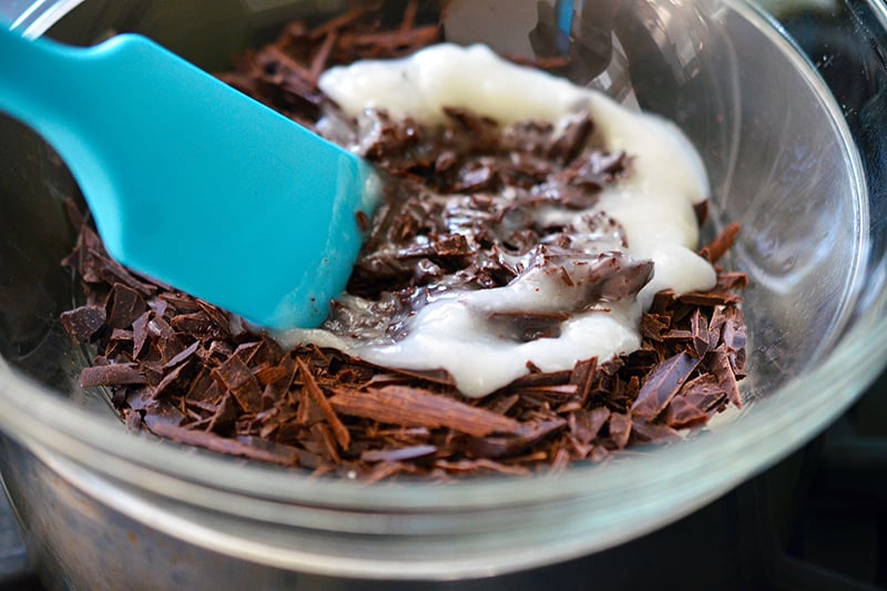 Sliced chocolate and coconut oil are being mixed in a glass bowl.