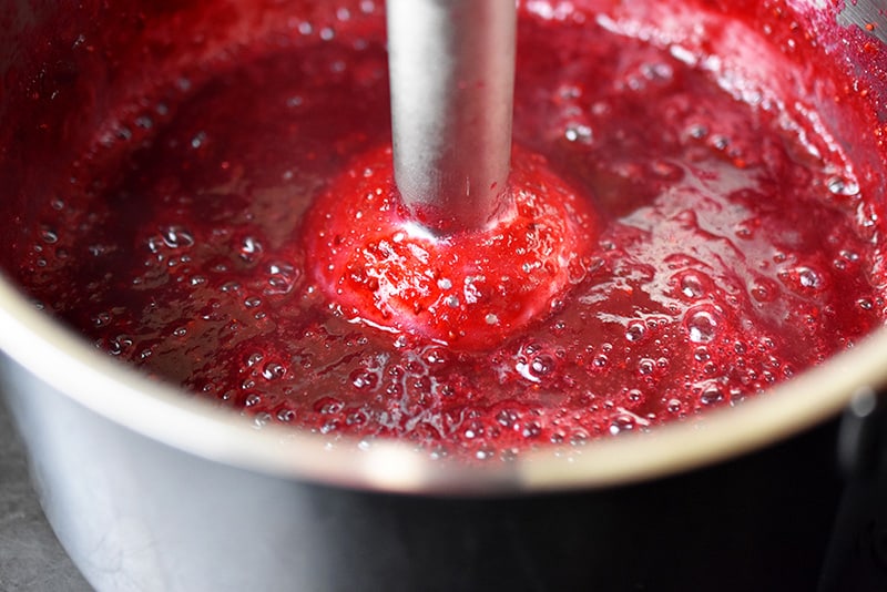 Someone using an immersion blender to mix the ingredients for paleo cran-cherry sauce together.