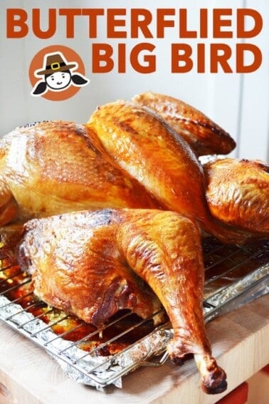 A golden brown spatchcock turkey is on a wire rack in a rimmed baking sheet.