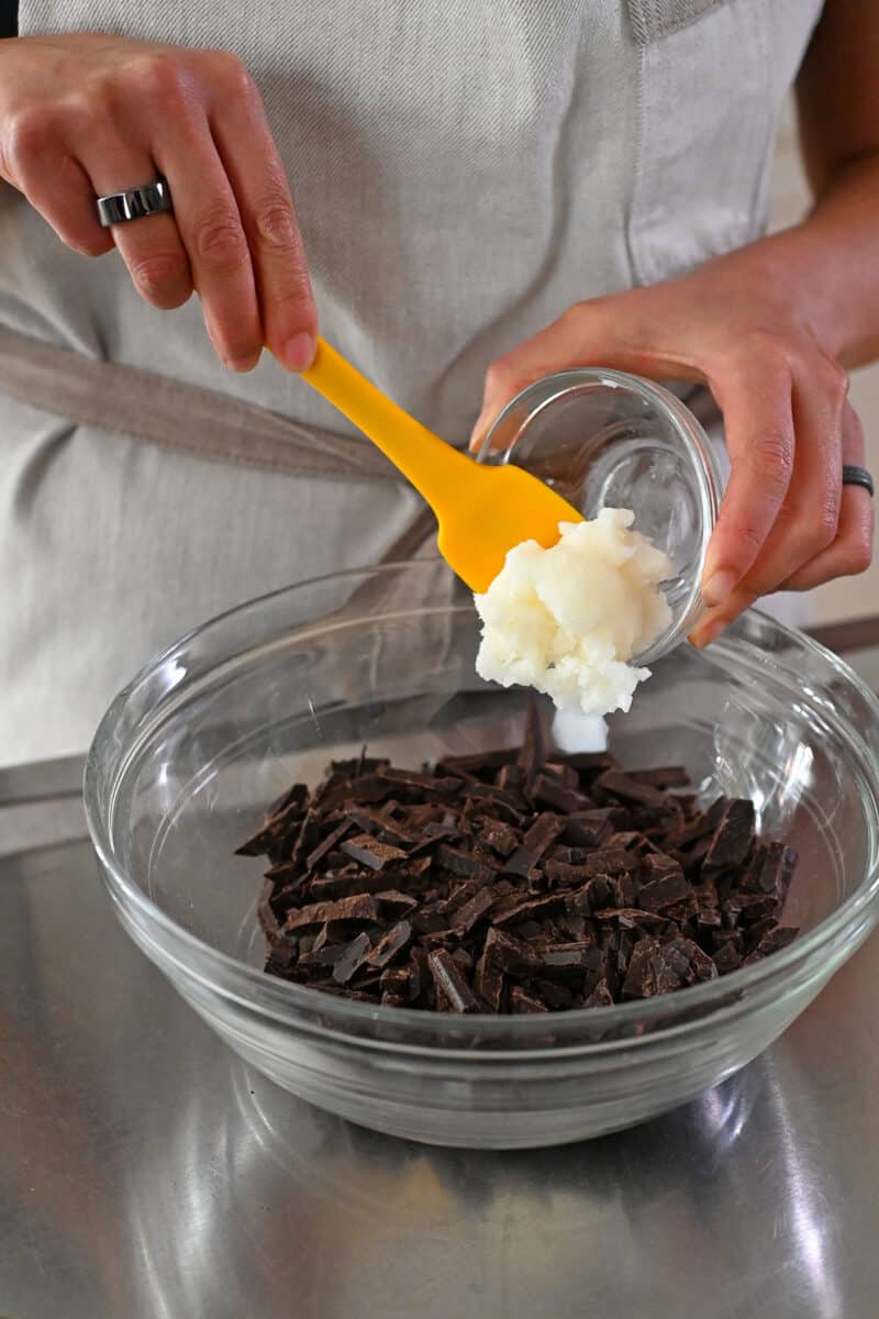 Adding refined coconut oil to a bowl with finely chopped up dark chocolate.