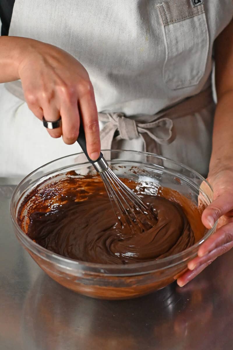 Whisking paleo and vegan chocolate ganache to make chocolate truffles in a clear glass bowl.