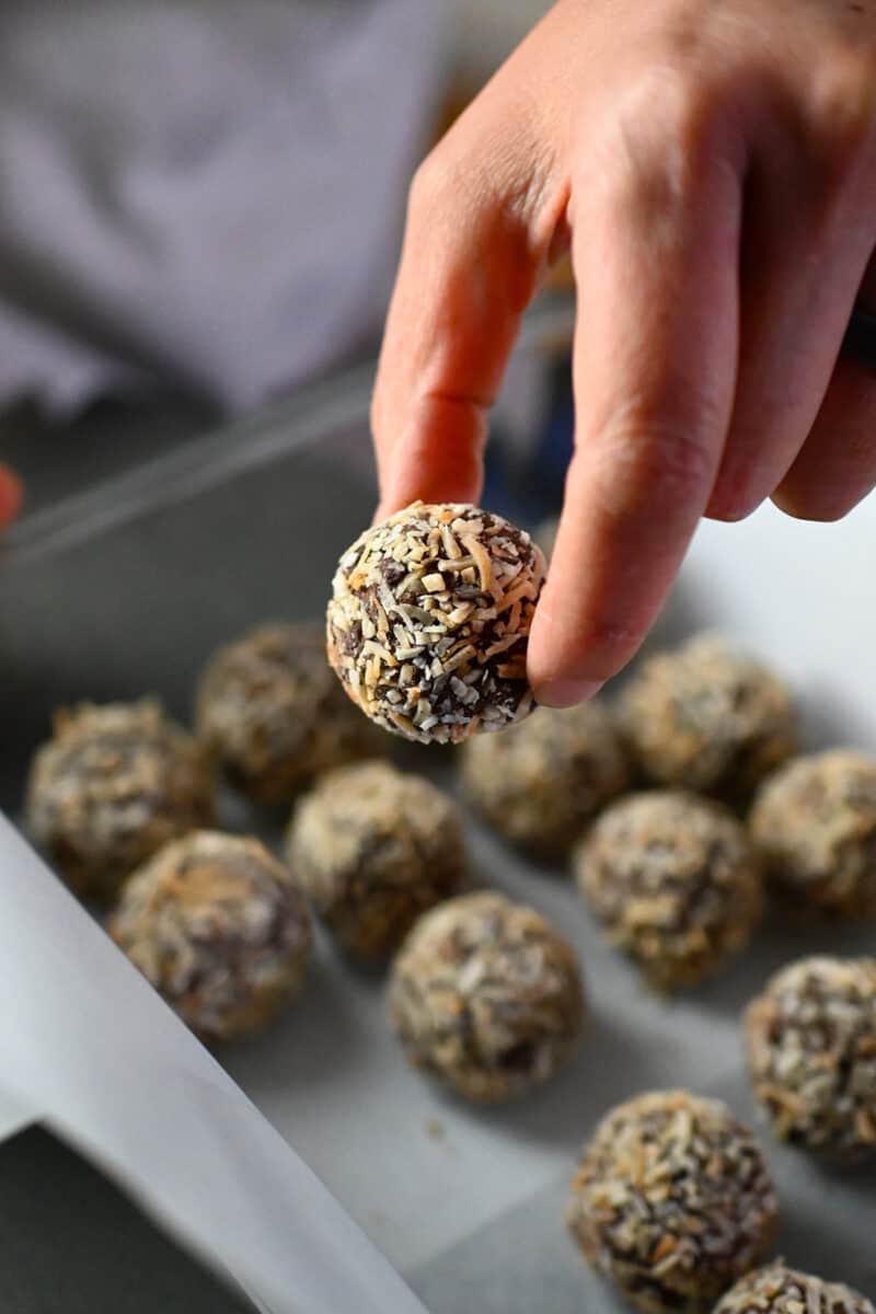 A hand is placing paleo truffles into a storage container lined with parchment paper.
