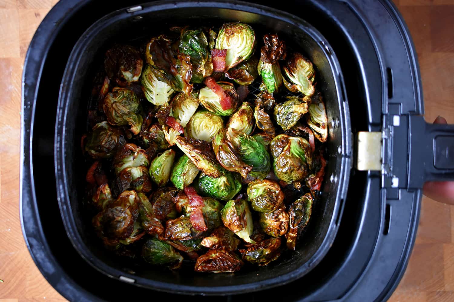 An overhead shot of an air fryer basket filled with crispy browned Brussels sprouts and bacon.