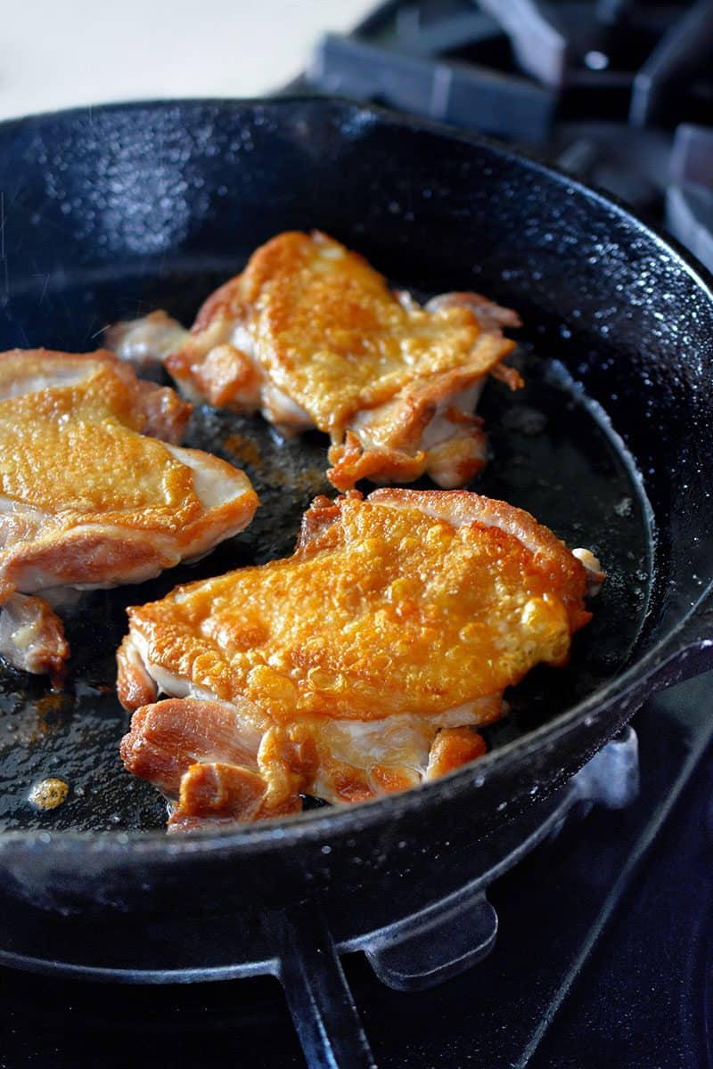 A closeup of crispy skinned Cracklin' Chicken frying in a cast iron skillet.