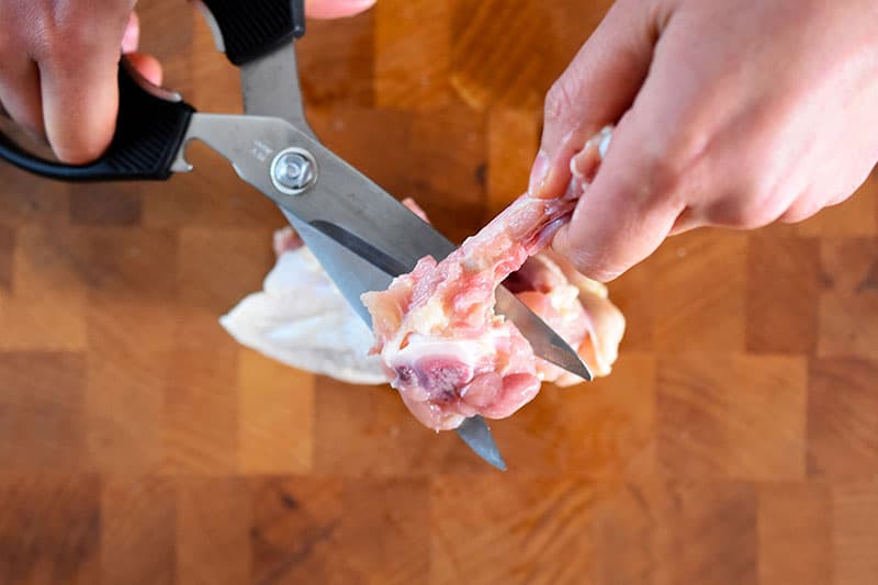 An overhead shot of removing the bone from the chicken thigh with a pair of kitchen shears.