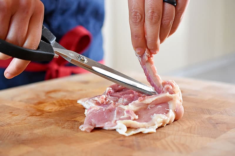 Using a pair of kitchen shears to remove the bone from a chicken thigh to make Cracklin’ Chicken 