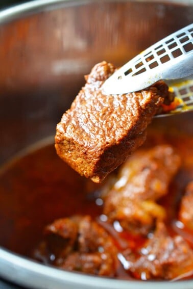 A pair of tongs is holding a piece of fork tender Instant Pot Mexican Beef