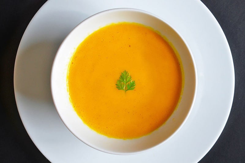 An overhead shot of Carrot Cardamom soup in a white bowl.