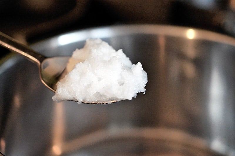 Adding a spoonful of coconut oil to a saucepan