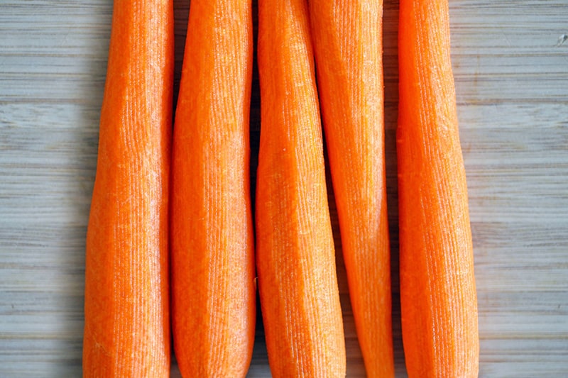 An overhead shot of five peeled carrots on a wooden cutting board.