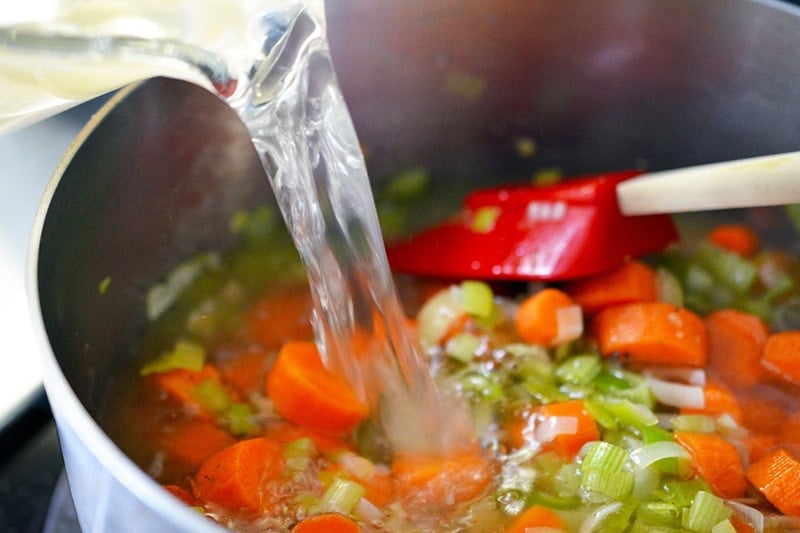 Pouring broth into the saucepan to make Carrot Cardamom Soup