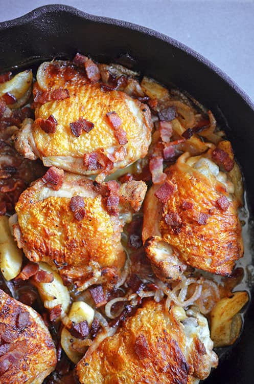 An overhead shot of a cast iron pan filled with pan-roasted chicken with bacon and apples