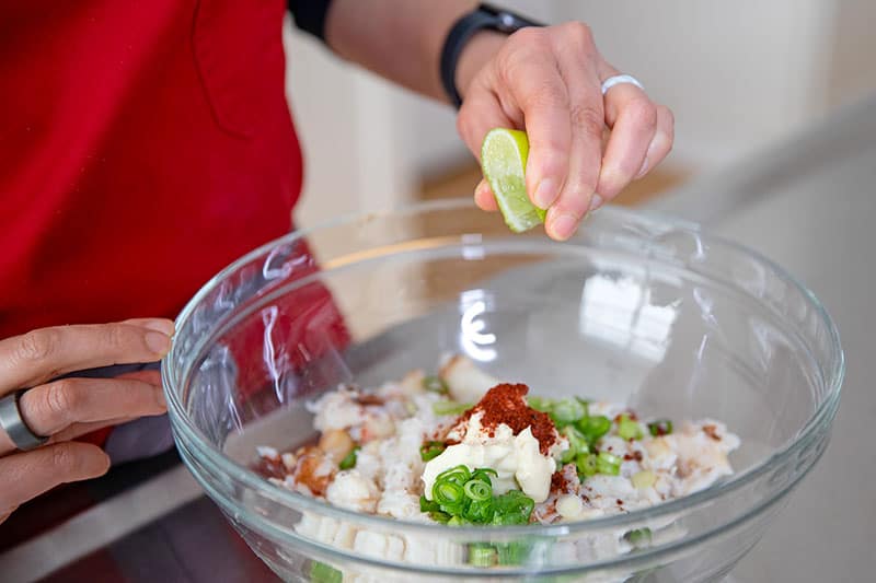 Squeezing lime juice into a bowl filled with the filling ingredients for Whole30 and keto California sushi hand rolls.