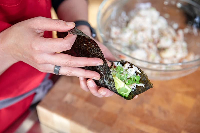 Wrapping the toasted nori around the filling to assemble a homemade California hand roll.