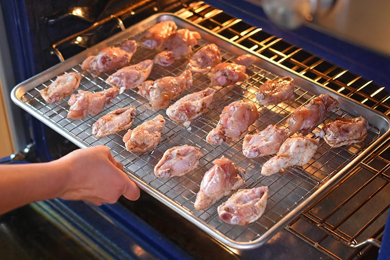 Someone putting a tray of magic wings into the oven to be cooked.