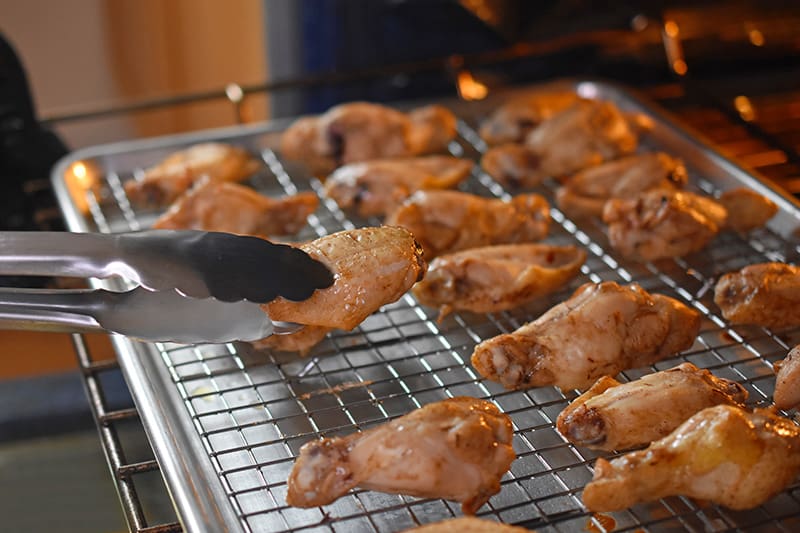 Flipping the baked chicken wings on the wire rack with a tong.