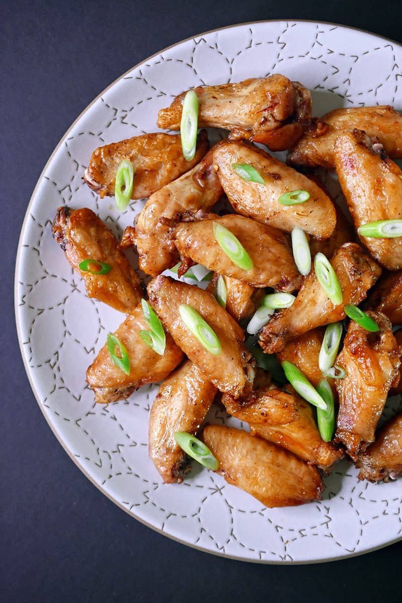 An overhead shot of a platter of baked chicken wings Magic Wings topped with sliced scallions.