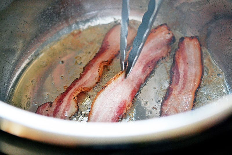 Frying three pieces of bacon in an Instant Pot.