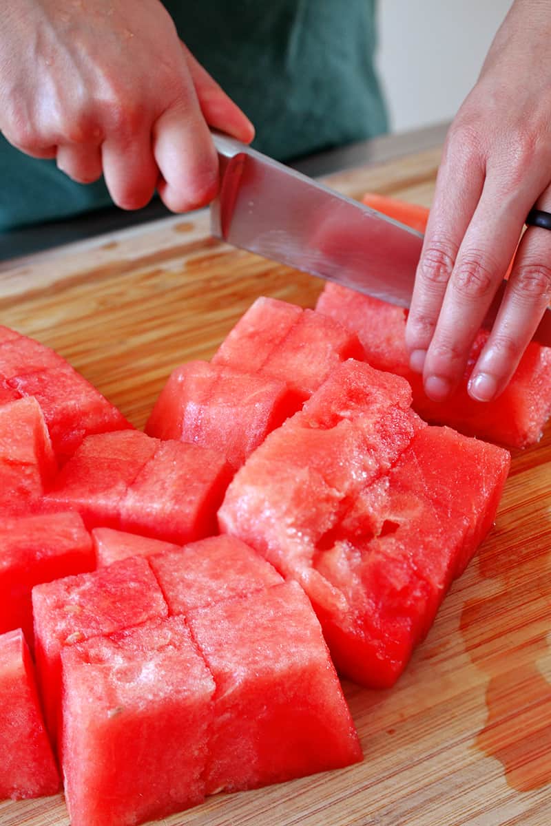 Cutting seedless watermelon into cubes on a wooden cutting board.