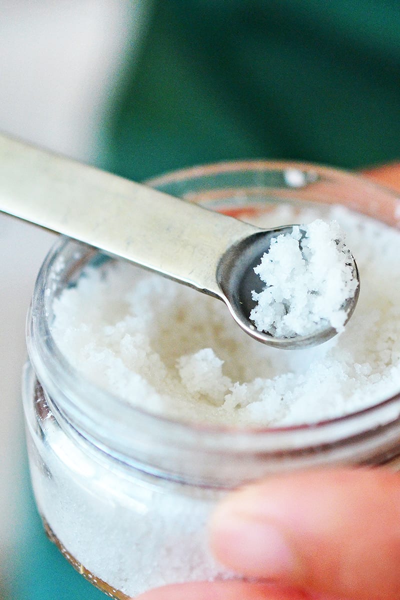 A measuring spoon scooping sea salt from a jar.