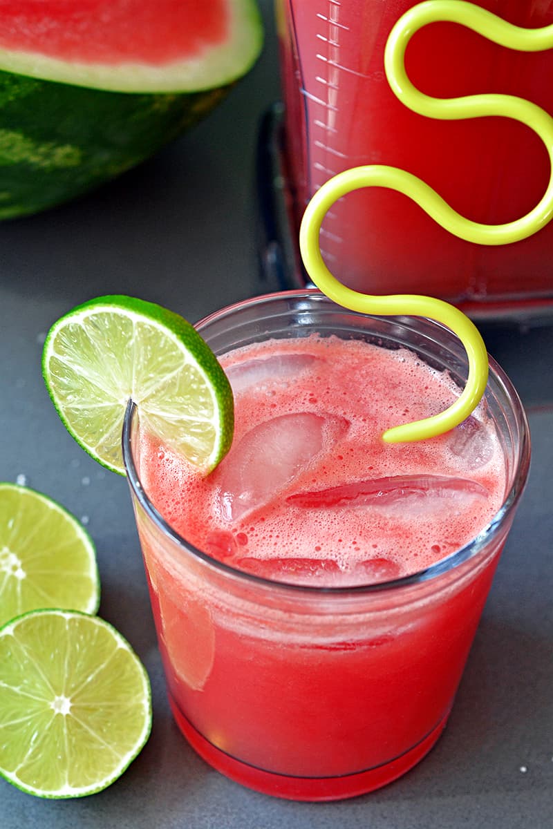 An overhead shot of watermelon juice cooler in a clear glass garnished with lime slices and a yellow straw.