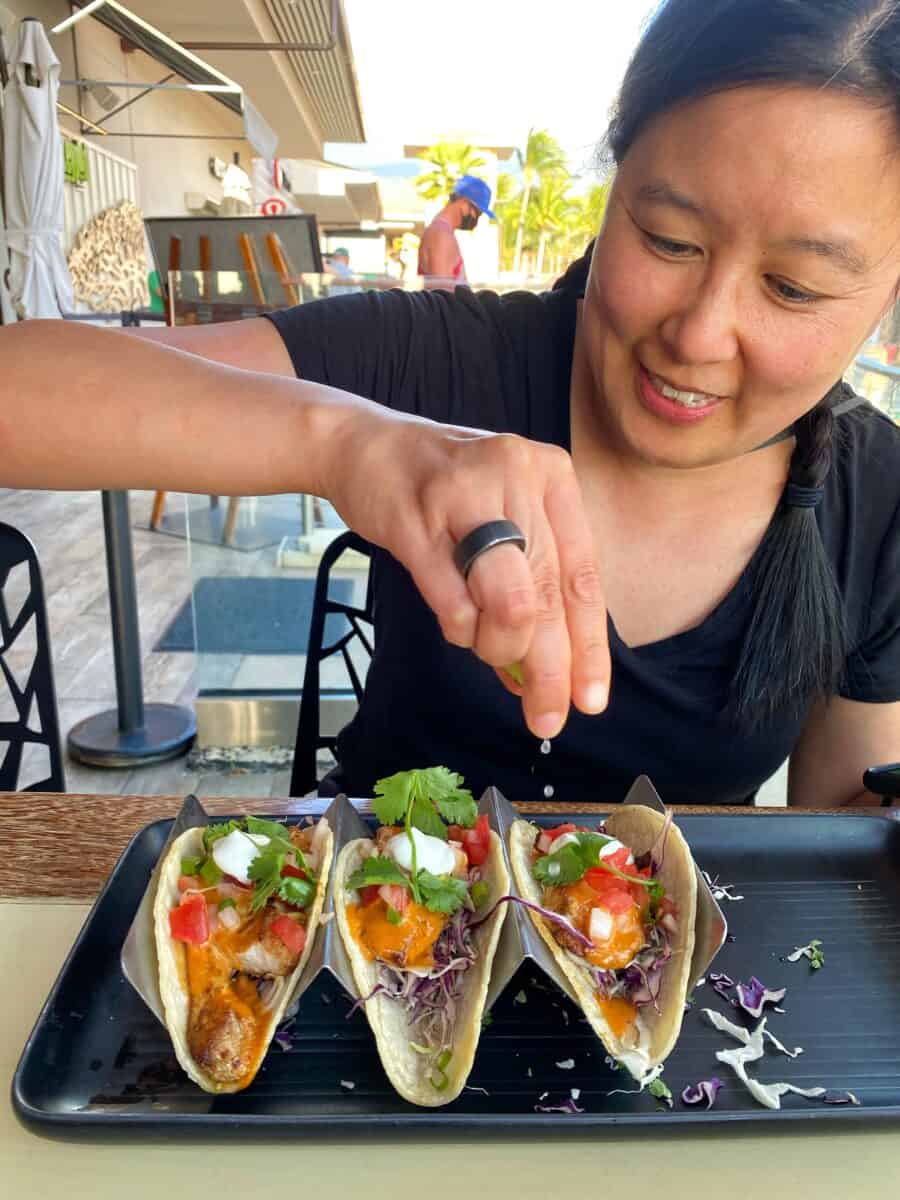 An Asian woman is squeezing lime juice on gluten-free fish tacos at Monkeypod in Maui