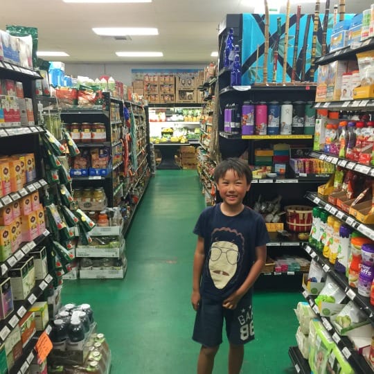 A smiling Asian boy is in the middle of a grocery store in Maui