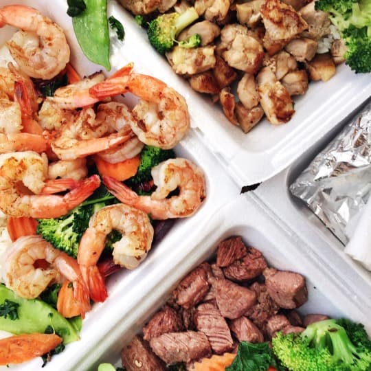 Overhead shot of takeout containers filled with shrimp, chicken, and steak dishes from Teppanyaki 2 Go.