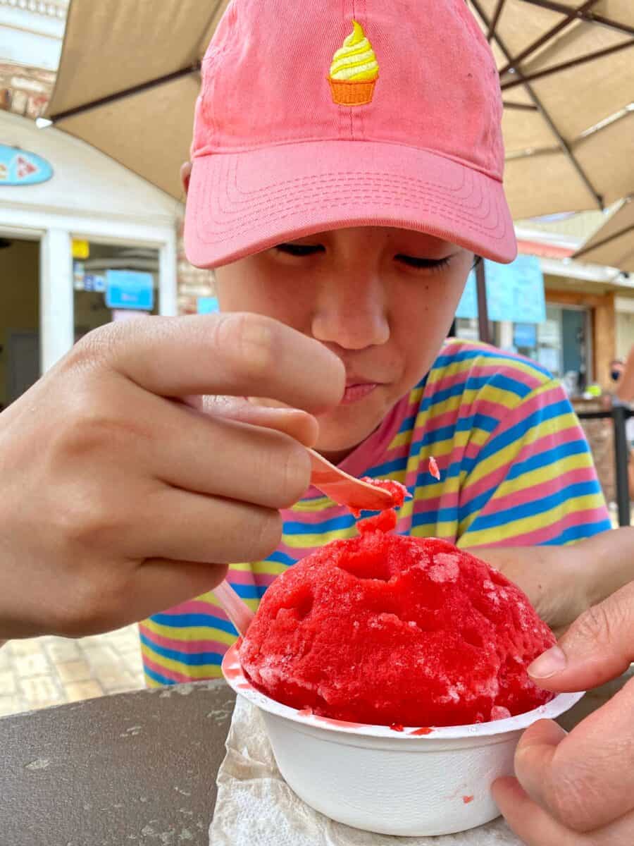 A boy in a pink hat is eating shave ice from Ululani's in Maui
