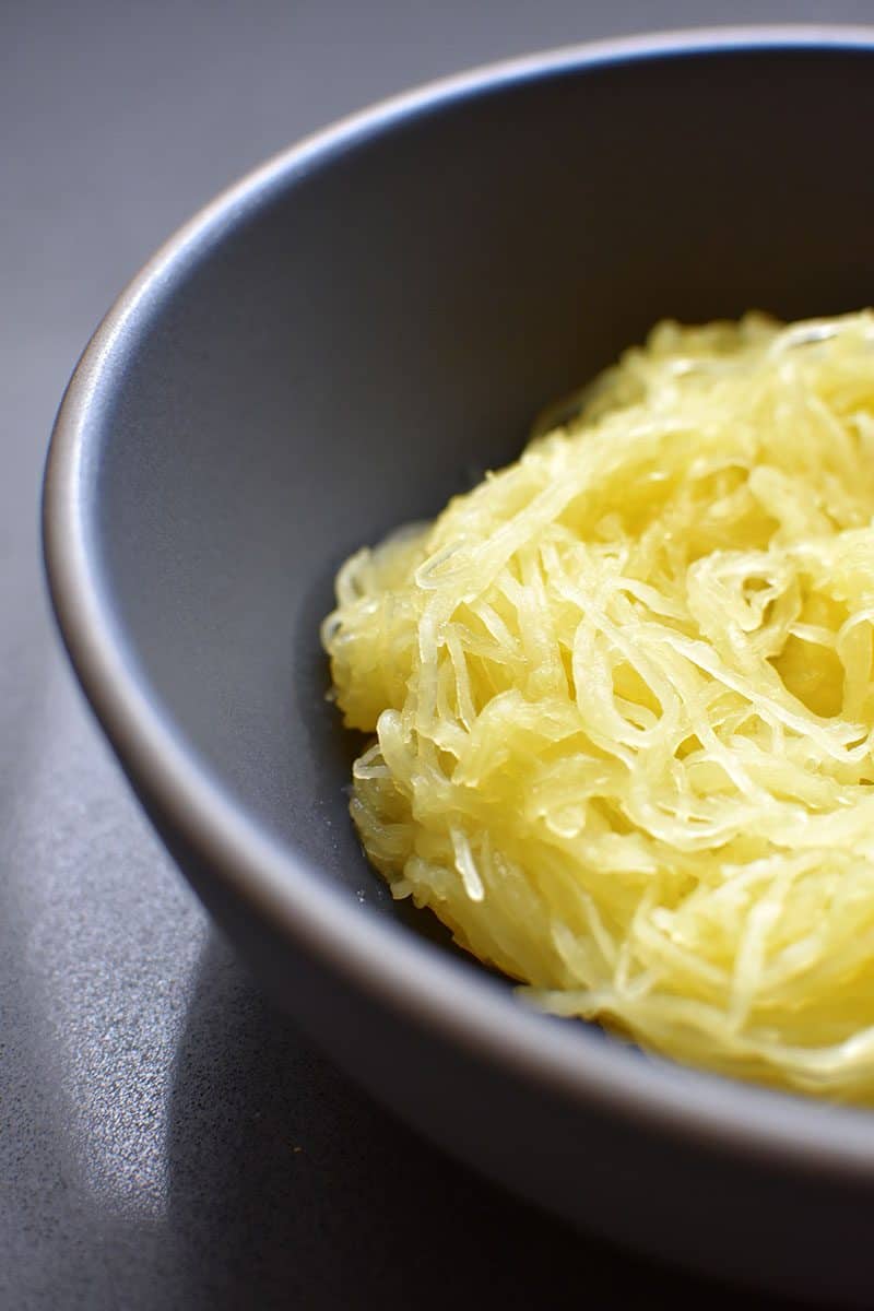 A close up of a blue-gray bowl filled with cooked spaghetti squash.