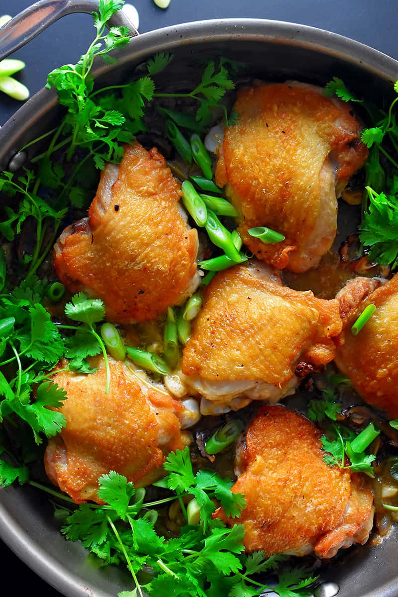 An overhead shot of Cantonese Crispy Chicken Thighs in a frying pan with fresh cilantro and scallions on top.