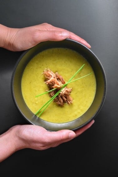 An overhead shot of someone holding a bowl of dairy-free Instant Pot Curried Cream of Broccoli Soup.