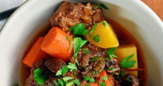 An overhead shot of a white bowl filled with paleo Instant Pot Beef stew with carrots and potatoes. There is a green and white napkin with a fork on top next to the bowl of stew.