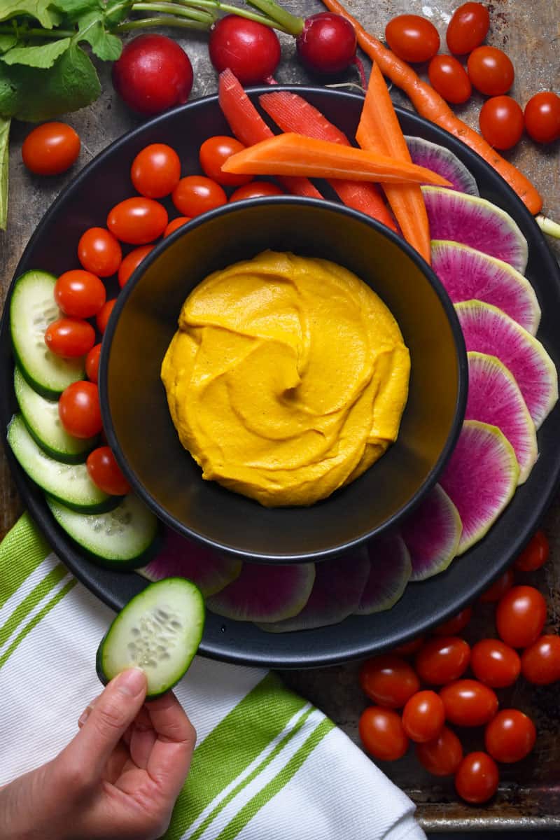 An overhead shot of a colorful platter of vegetables surrounding a bowl of vegan and Whole30 sweet potato and cashew dip.