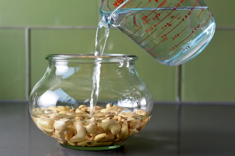 Someone pouring water in a bowl with cashews to soak.