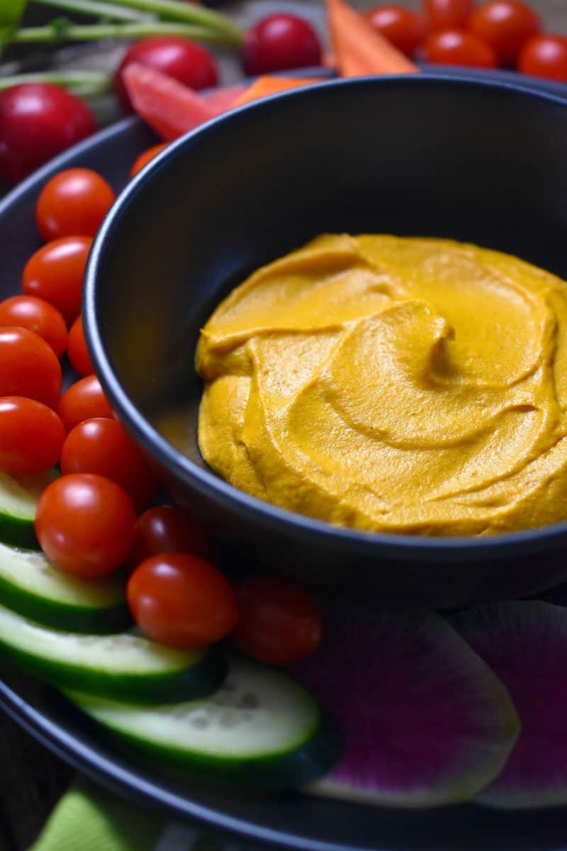A bowl of the sweet potato and cashew dip surrounded by an array of vegetables.