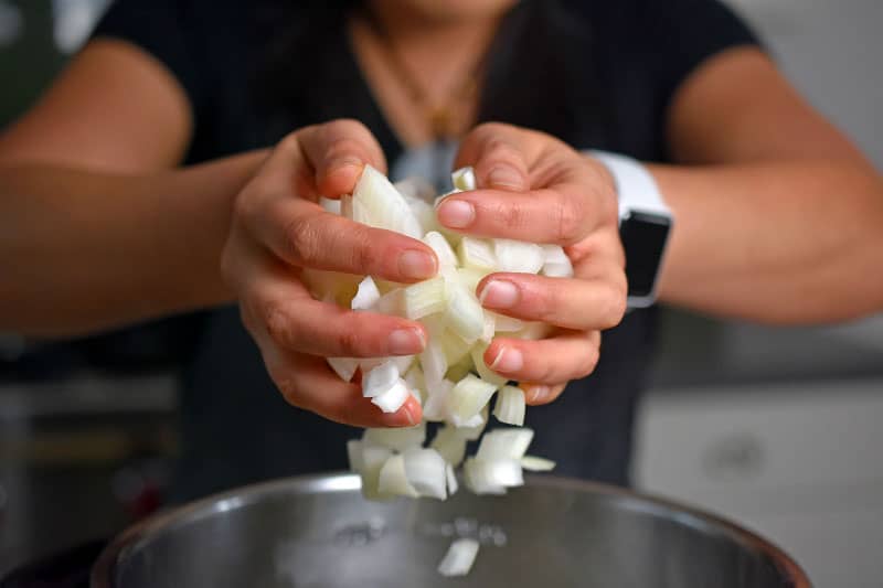 Two hands adding chopped onions to an open Instant Pot.