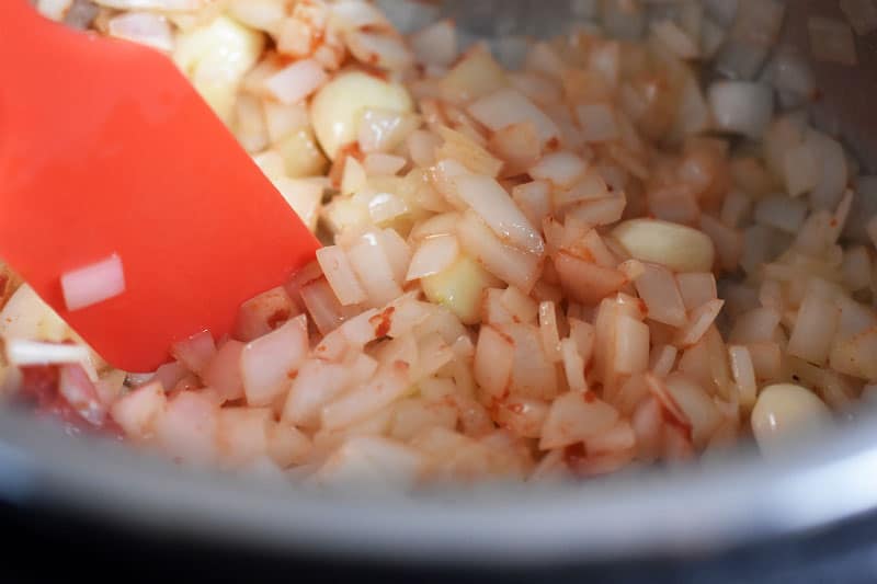 A closeup shot of chopped onions and tomato paste sautéing in an Instant Pot.