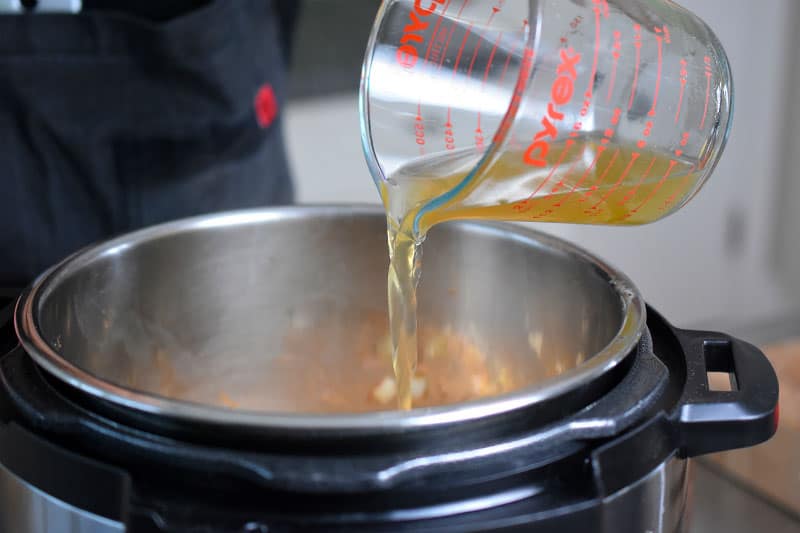 Chicken broth is poured from a liquid measuring cup into an Instant Pot.